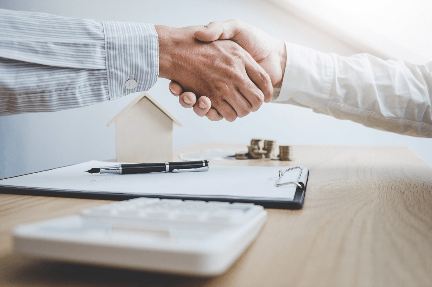 Two men are shaking hands over a clipboard with a house in the background.