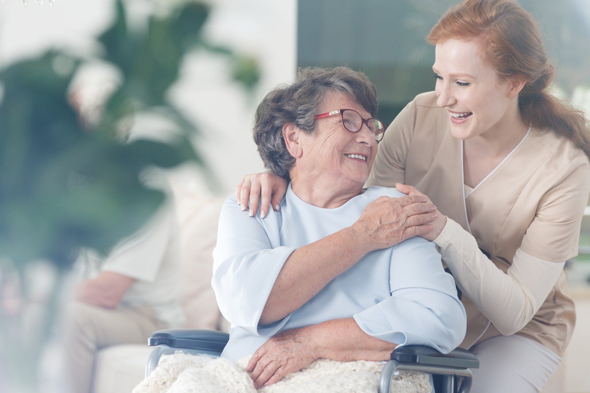 A nurse is hugging an elderly woman in a wheelchair.